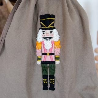 Nahaufnahme: gestickter Nussknacker in Pink mit weißem Bart auf dem Geschenkbeutel