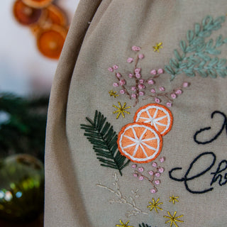 Nahaufnahme: gestickte Orangenscheiben, rosa Beeren und goldene Sterne auf dem Geschenkbeutel