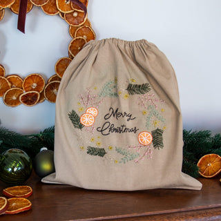 Geschenkbeutel Orangenkranz, fertig bestickt mit Merry Christmas, vor einem Kranz aus getrockneten Orangen