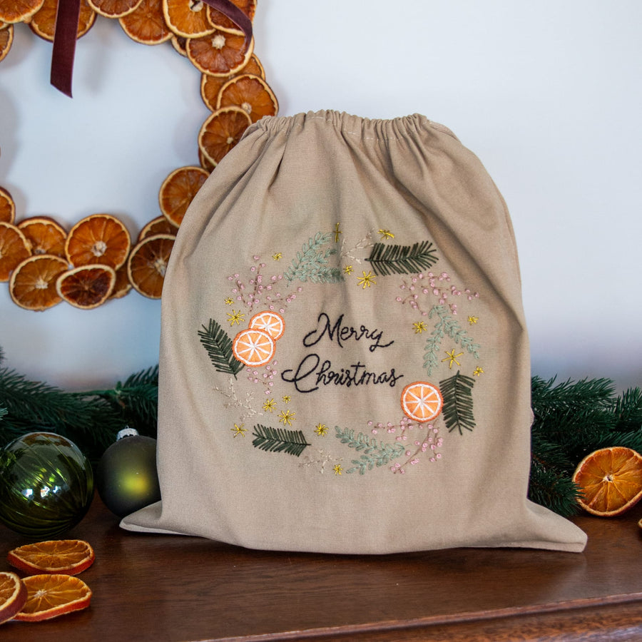 Geschenkbeutel Orangenkranz, fertig bestickt mit Merry Christmas, vor einem Kranz aus getrockneten Orangen